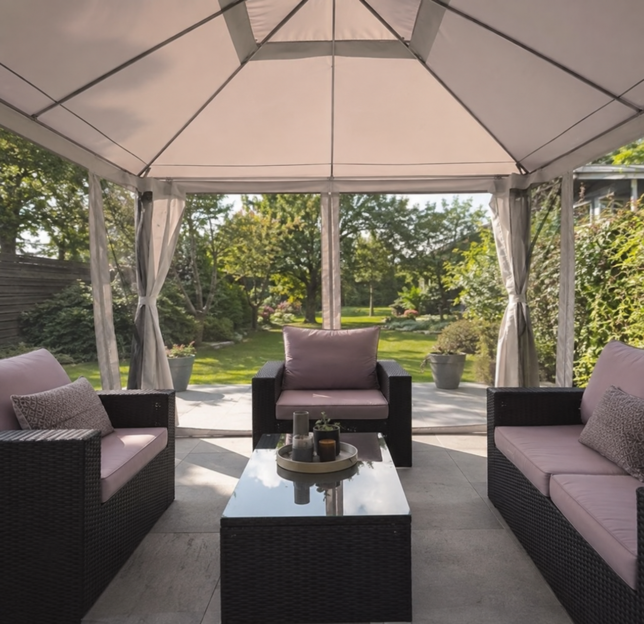 View from inside a PAVEA Haven gazebo looking out over a green garden, with lounge seating under the canopy